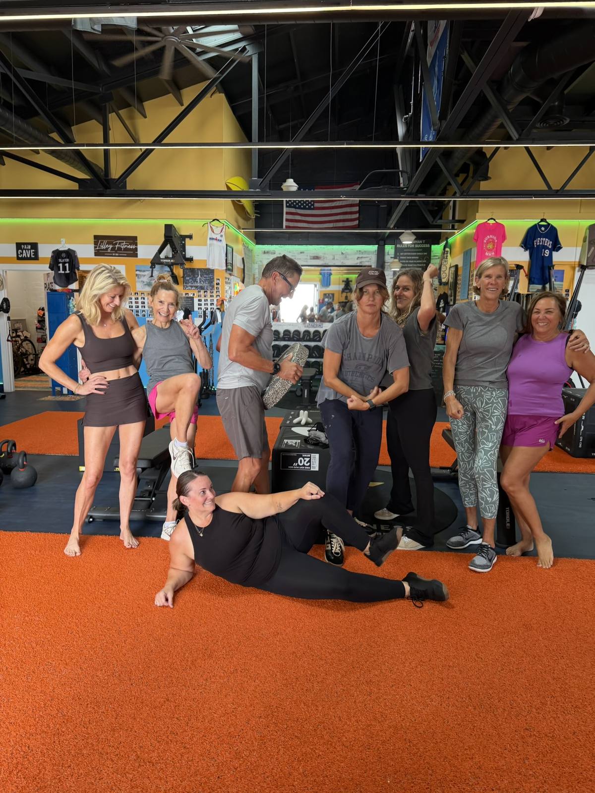 A playful group of adult members flexing on the orange turf, one of them lying on the floor.