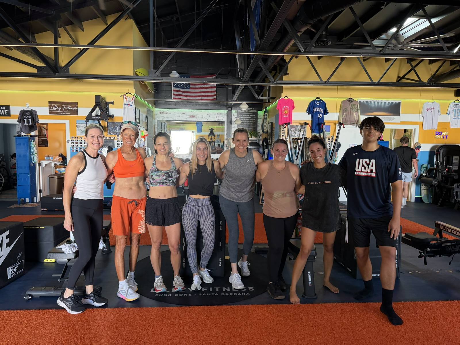 A group of Lilley Fitness members, mostly women of different ages and a teen, standing on the training floor by the Lilley Fitness Funk Zone mat.