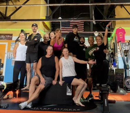 A small group of adult members gathered on and around a plyo box in the gym.