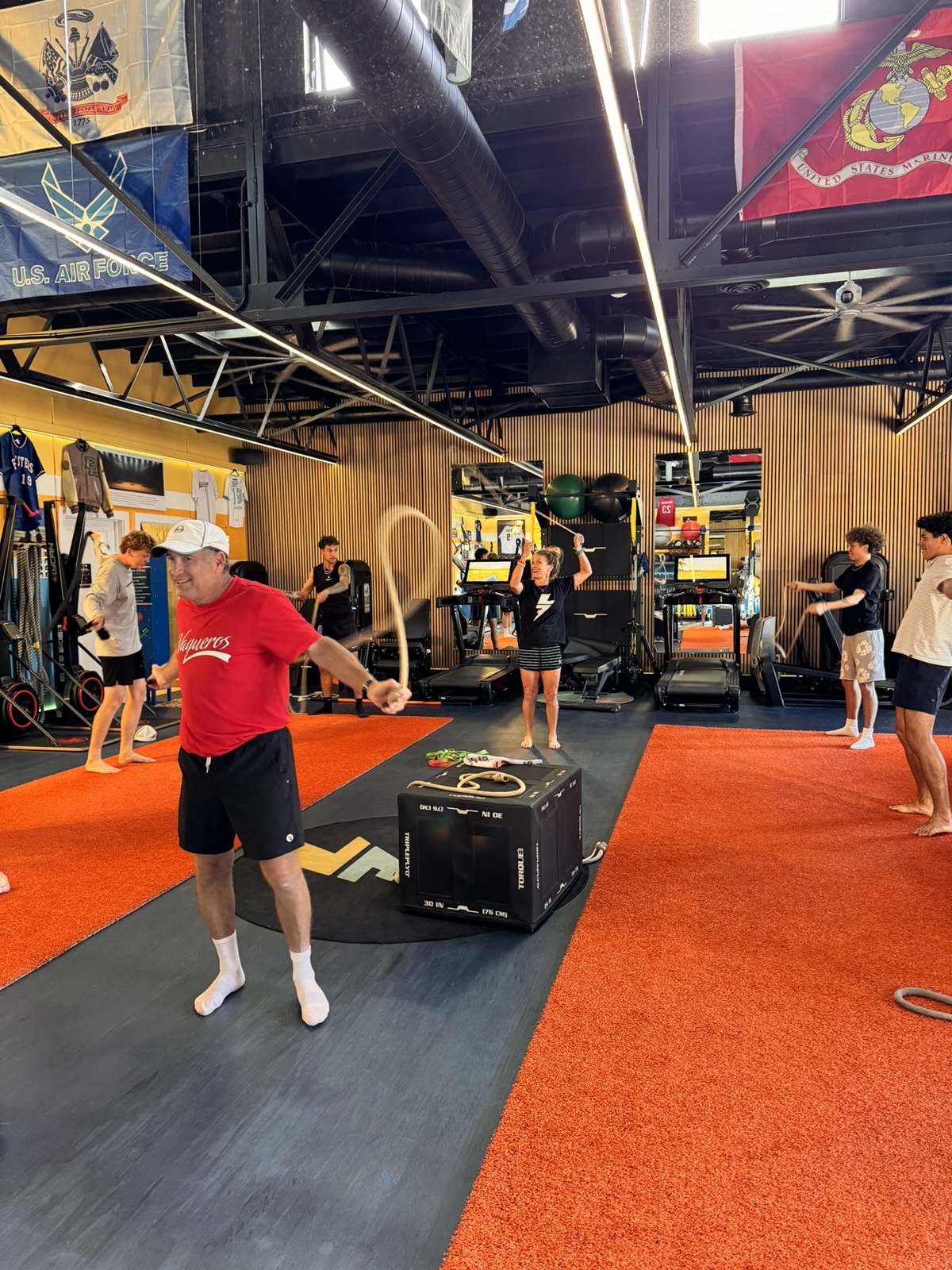 A member jumping rope in a Lilley Fitness class, with Erika and young athletes behind him.